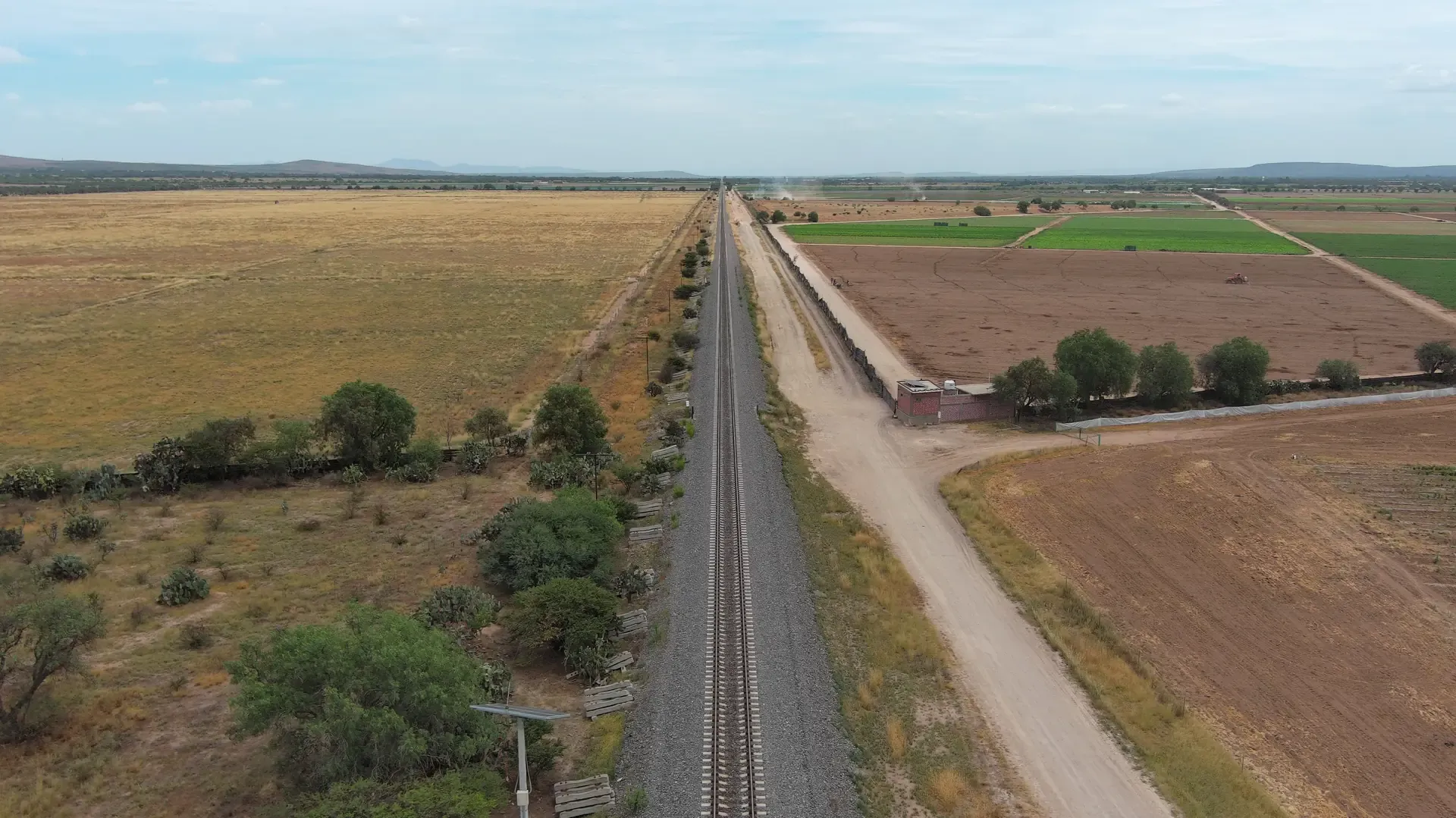 Vía férrea con canal y campos de cultivo, fotografía aérea 4K